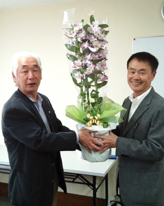 写真は、優勝者 笹平邦比古さん（右）　同窓会 長岡副会長が祝花を贈呈